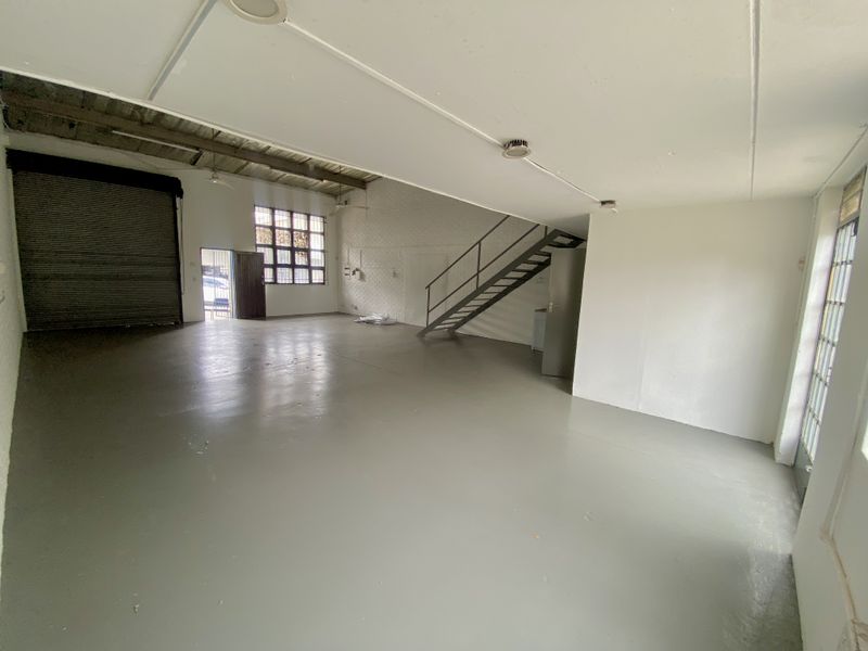 Spacious industrial utility area featuring a roller shutter door, steel staircase, and exposed ceiling beams, suitable for workshop or storage use.