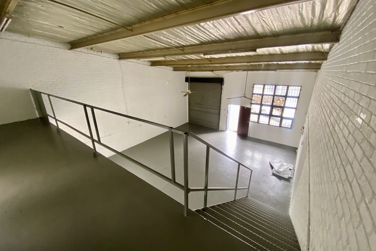 Spacious industrial open-plan unit featuring a mezzanine level, painted brick walls, exposed steel roof structure, and a large roller shutter door for easy access.