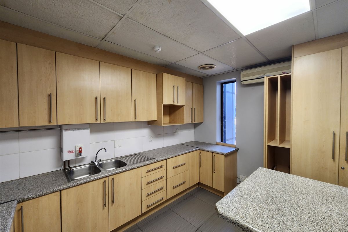 A functional office kitchenette featuring light wood cabinetry, granite-look laminate countertops, a stainless steel sink, and a wall-mounted water heater.