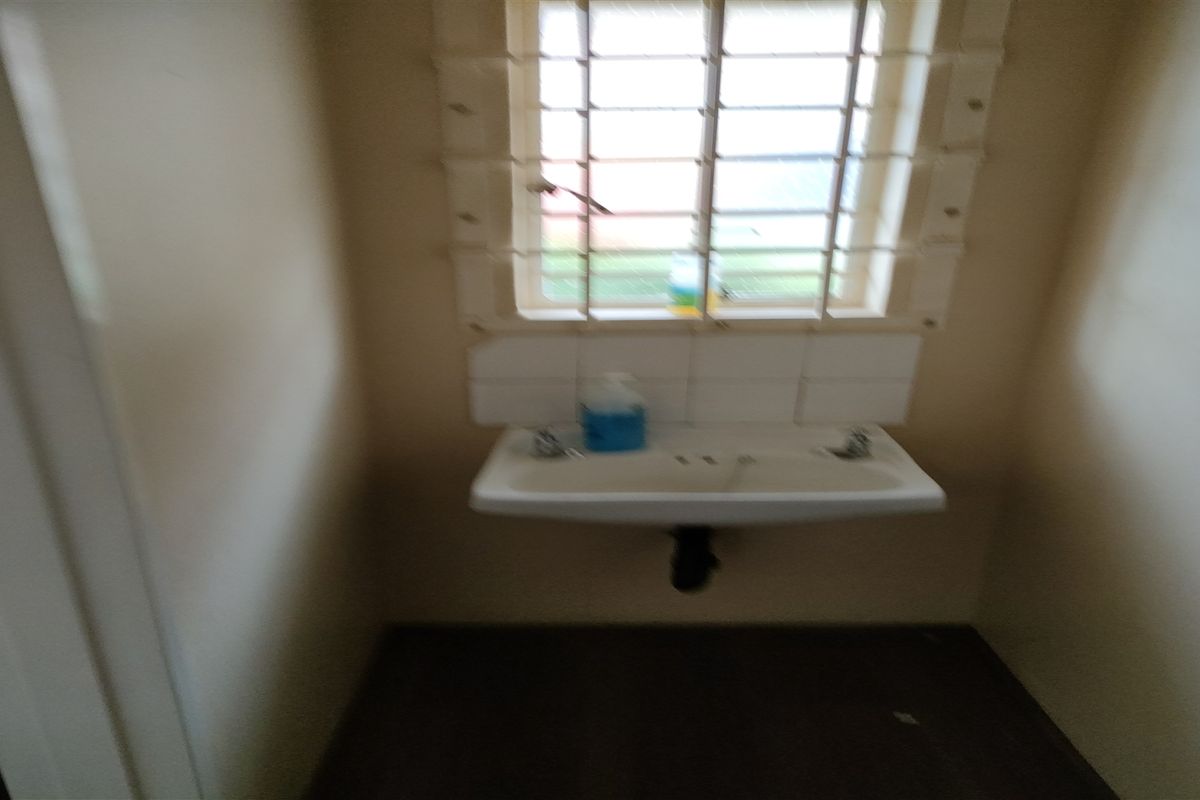 A small, empty bathroom featuring a wall-mounted basin with a tiled splashback and a window fitted with security bars.