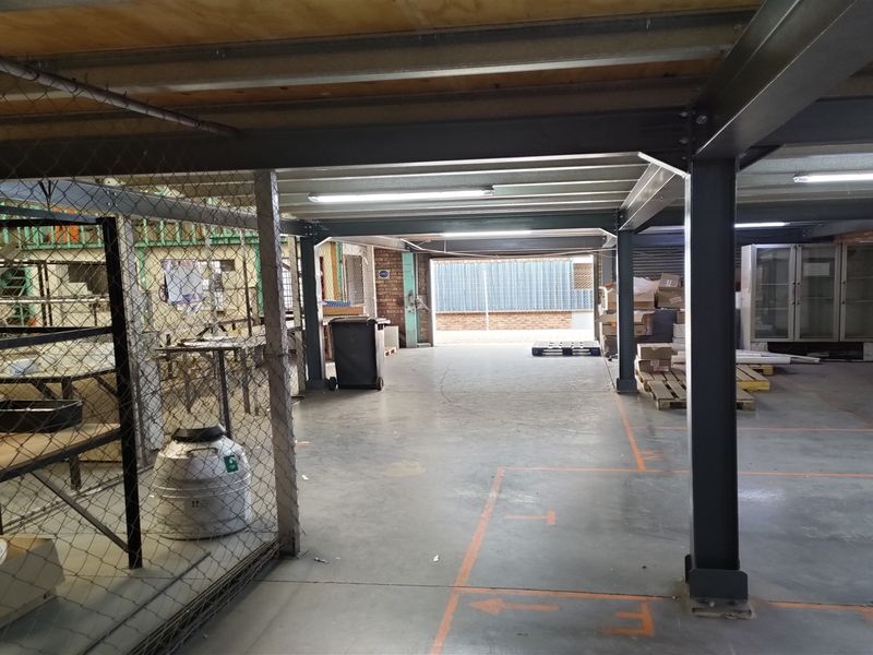 Spacious industrial utility area featuring a steel mezzanine structure, concrete flooring, and wire mesh partitioning, suitable for storage or workshop operations.