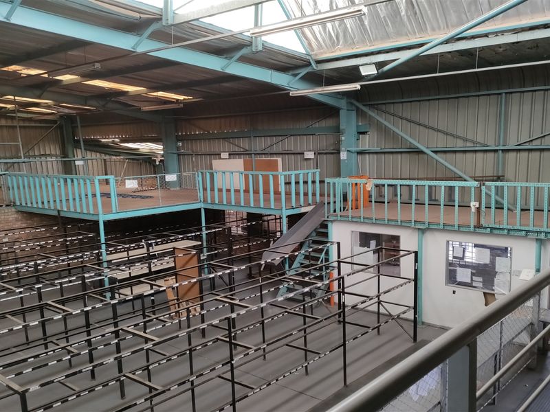 Spacious industrial warehouse featuring a mezzanine level, high ceilings with integrated skylights, and extensive steel racking infrastructure suitable for storage or manufacturing operations.