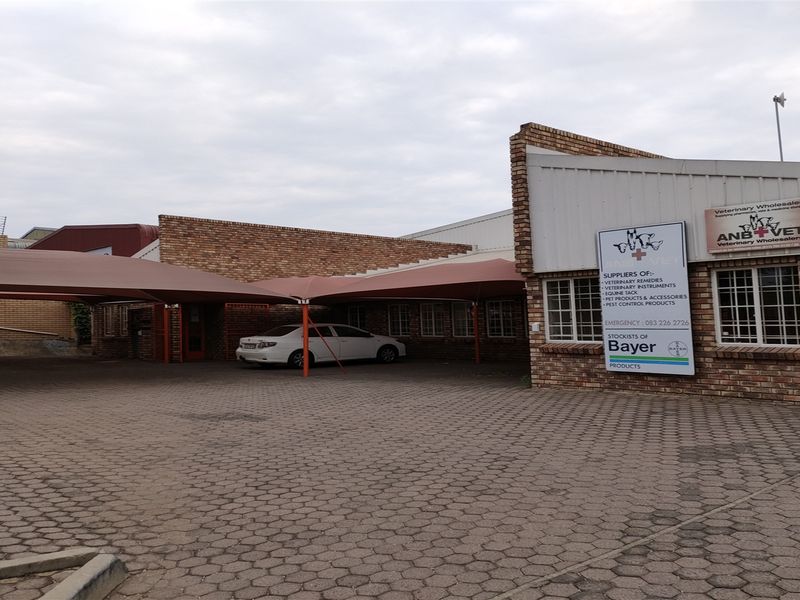 Front exterior view of an industrial property featuring a paved driveway, shade cloth carport, and brick facade with commercial signage.