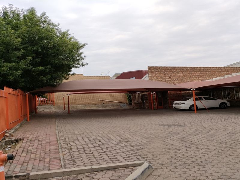 Industrial property exterior featuring a paved driveway with shade cloth carports, brick facade, and secure metal perimeter fencing.