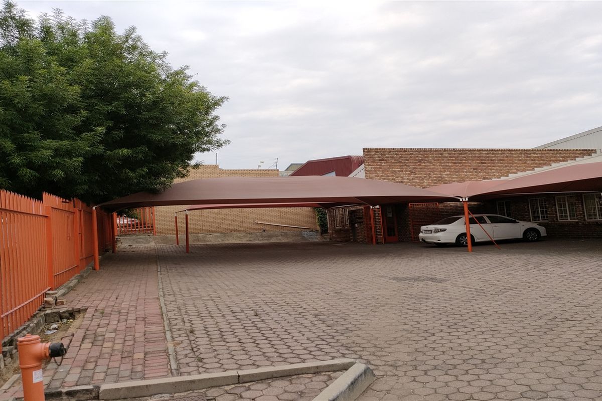 Industrial property exterior featuring a paved driveway with shade cloth carports, brick facade, and secure metal perimeter fencing.