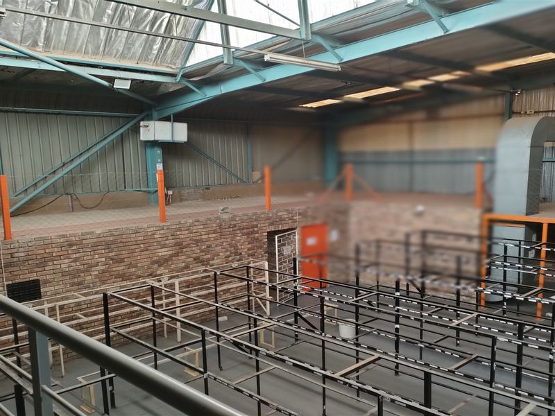 Spacious industrial utility area featuring a mezzanine level, exposed steel roof trusses, and functional ventilation ducting, suitable for warehouse or manufacturing operations.