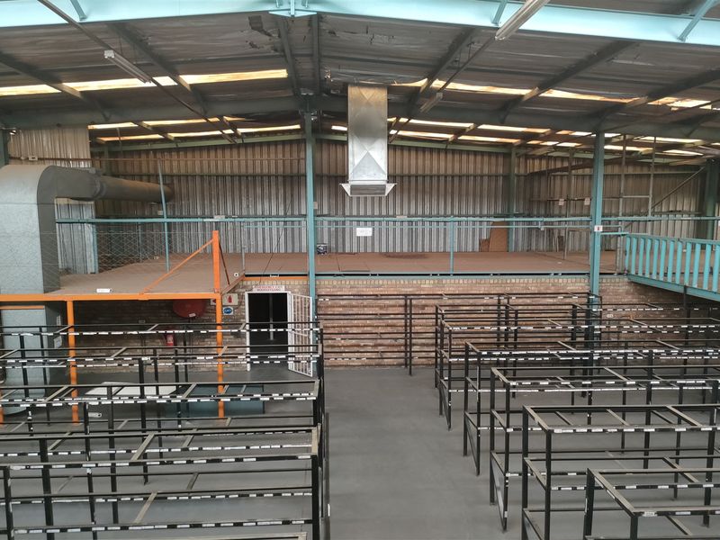 Spacious industrial warehouse area featuring a mezzanine level, exposed metal roof structure, ventilation ducting, and durable concrete flooring suitable for various commercial operations.