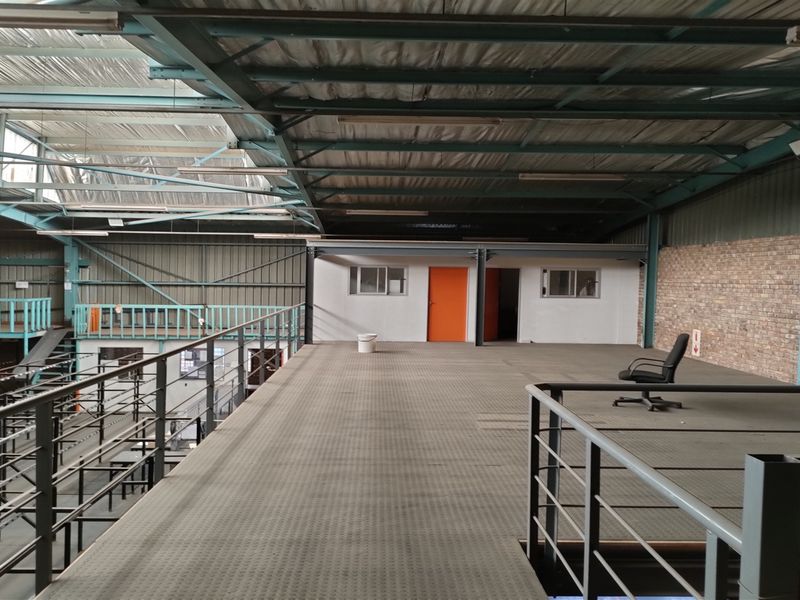 Spacious industrial mezzanine level featuring exposed steel roof trusses, brick wall detailing, and metal balustrades, suitable for storage or office conversion.
