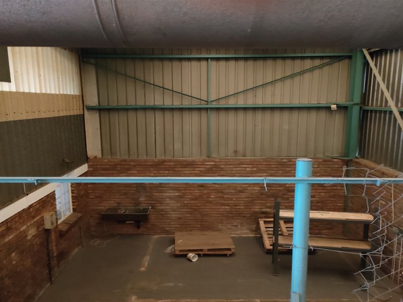 An industrial utility space featuring exposed brick walls, corrugated metal cladding, concrete flooring, and overhead ventilation ducting, suitable for storage or workshop use.