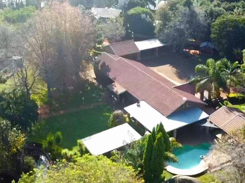 Aerial view of a small holding property featuring a main residence with a tiled roof, swimming pool, covered patio, and expansive garden grounds.