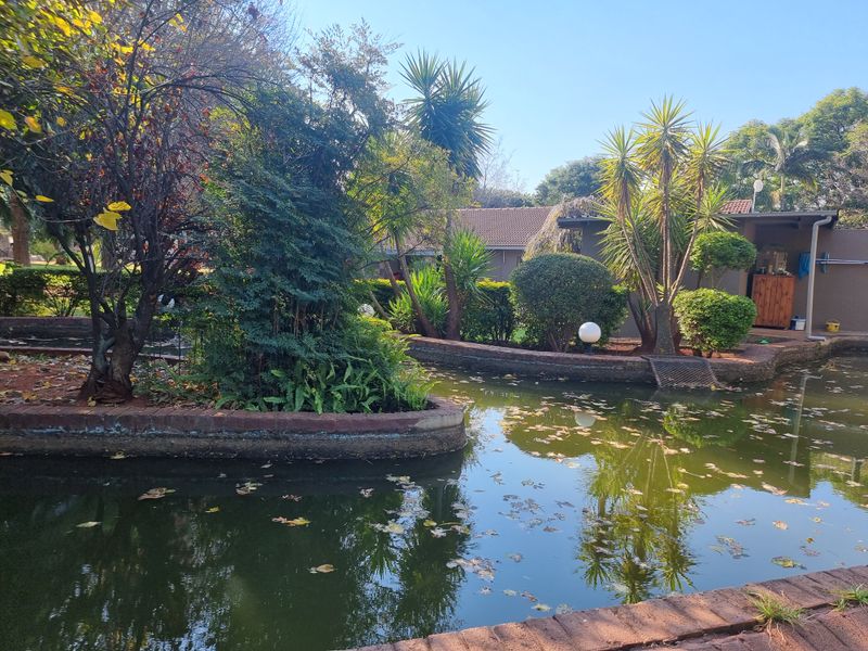 A landscaped garden area featuring a large brick-lined pond with mature trees and shrubs, providing a tranquil outdoor setting.