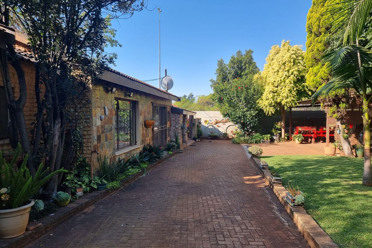 A well-maintained rear exterior view of the small holding featuring a brick-paved driveway, stone-clad building facade, and established garden area.