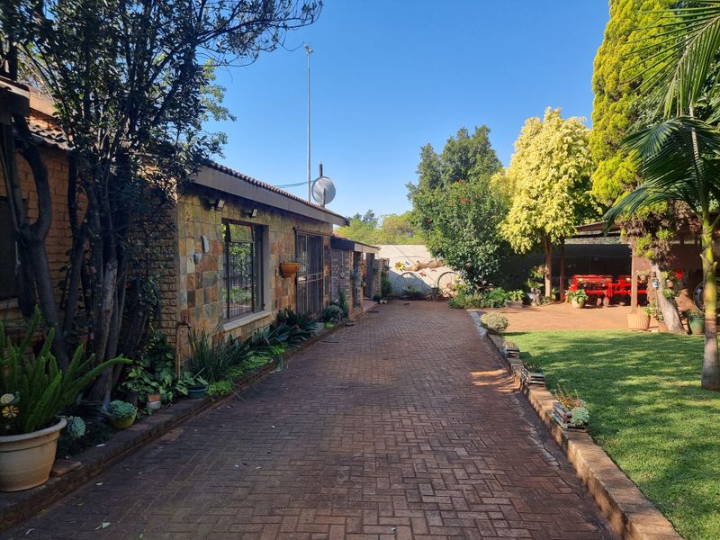 A well-maintained rear exterior view of the small holding featuring a brick-paved driveway, stone-clad building facade, and established garden area.
