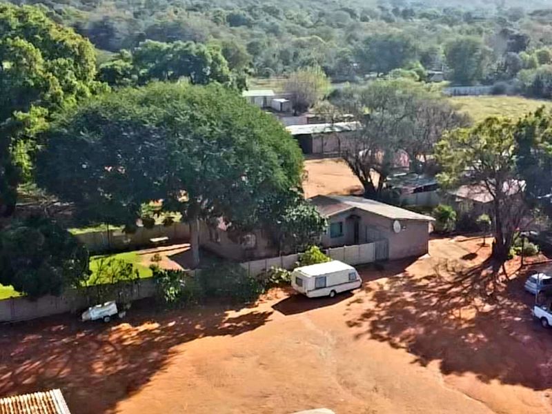 Aerial view of a small holding property featuring expansive grounds, mature trees, perimeter fencing, and multiple outbuildings on a large plot.