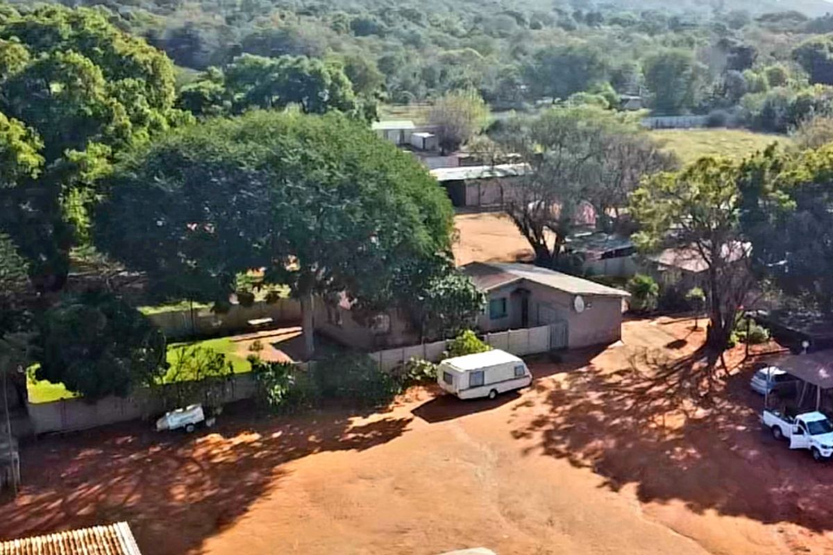 Aerial view of a small holding property featuring expansive grounds, mature trees, perimeter fencing, and multiple outbuildings on a large plot.
