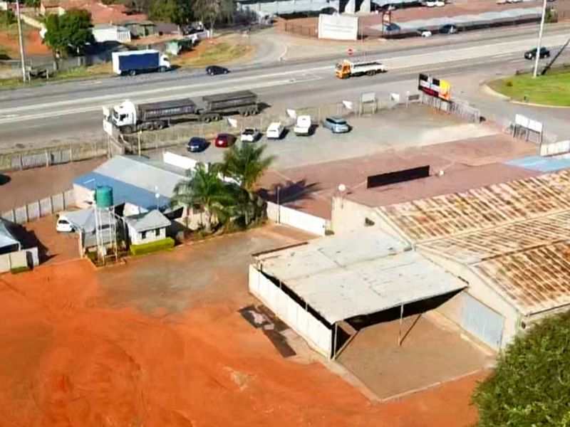 Aerial view of the small holding property featuring multiple structures, corrugated metal roofing, water storage, and paved parking areas adjacent to a main road.