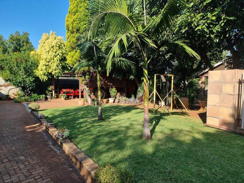 A well-maintained garden area featuring a manicured lawn, mature palm trees, and a paved walkway with stone-clad structural elements.