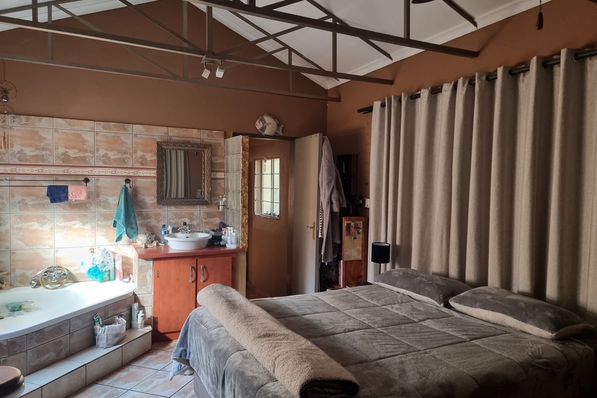Spacious bedroom featuring exposed roof trusses, an integrated vanity with vessel sink, and a tiled bathtub area.