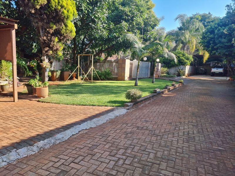 A well-maintained garden area featuring a brick-paved driveway, established trees, and a neat lawn, providing a pleasant outdoor entrance to the property.