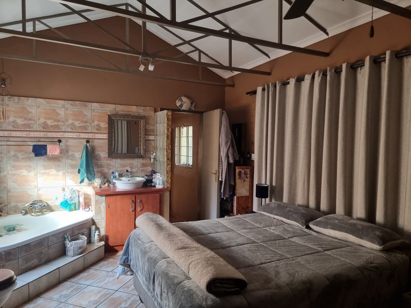 Spacious bedroom featuring exposed roof trusses, an integrated vanity with vessel sink, and a tiled bathtub area.