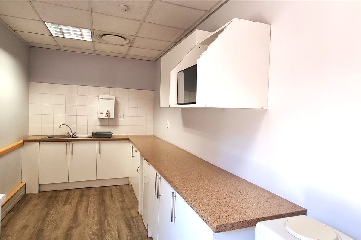 A functional office kitchenette featuring laminate countertops, built-in cabinetry, a stainless steel sink, and a suspended ceiling with integrated lighting.