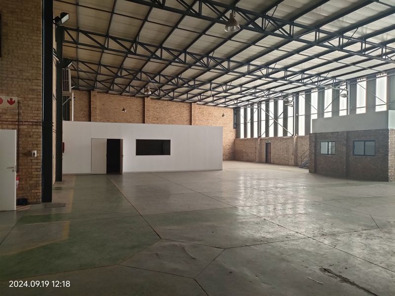 Spacious industrial warehouse featuring high ceilings with exposed steel trusses, concrete flooring, and an internal office partition, suitable for various commercial or storage uses.