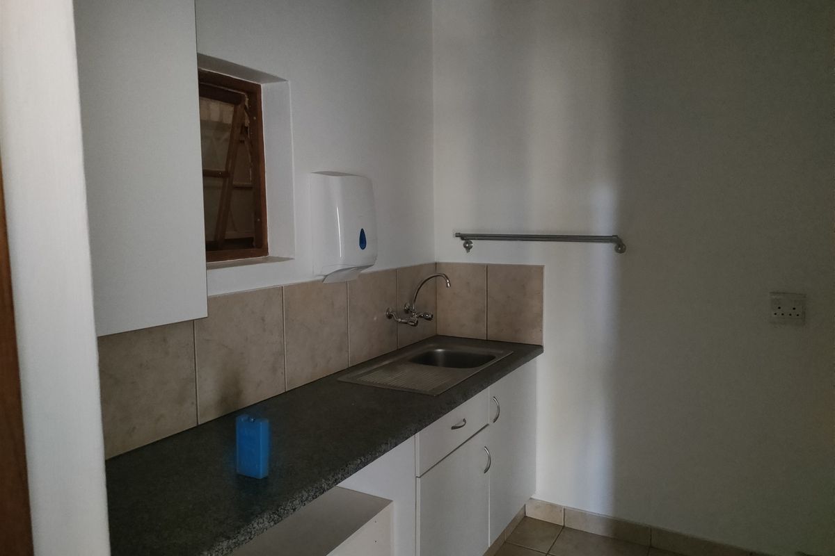 A functional kitchenette area featuring a stainless steel sink, tiled backsplash, laminate countertop, and built-in cabinetry, suitable for office or industrial utility use.