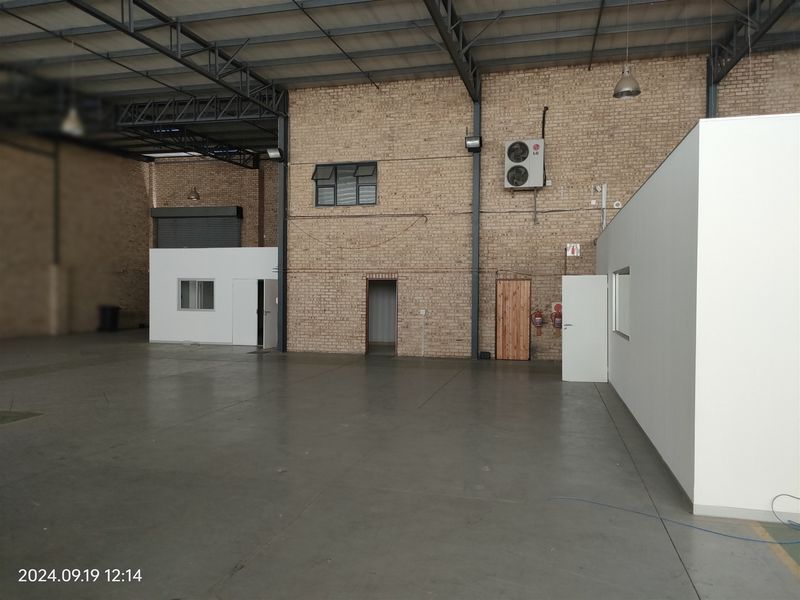 Spacious industrial warehouse unit featuring high ceilings with exposed steel trusses, durable concrete flooring, facebrick walls, and integrated office partitioning.