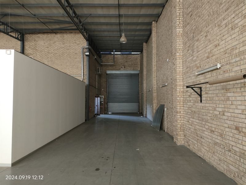 Spacious industrial utility area featuring high ceilings with exposed steel trusses, durable concrete flooring, and a large roller shutter door for easy access.