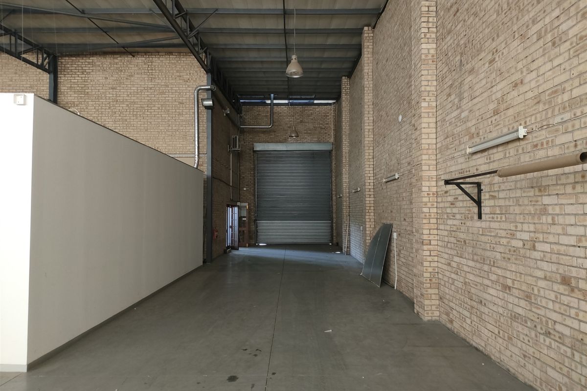 Spacious industrial utility area featuring high ceilings with exposed steel trusses, durable concrete flooring, and a large roller shutter door for easy access.