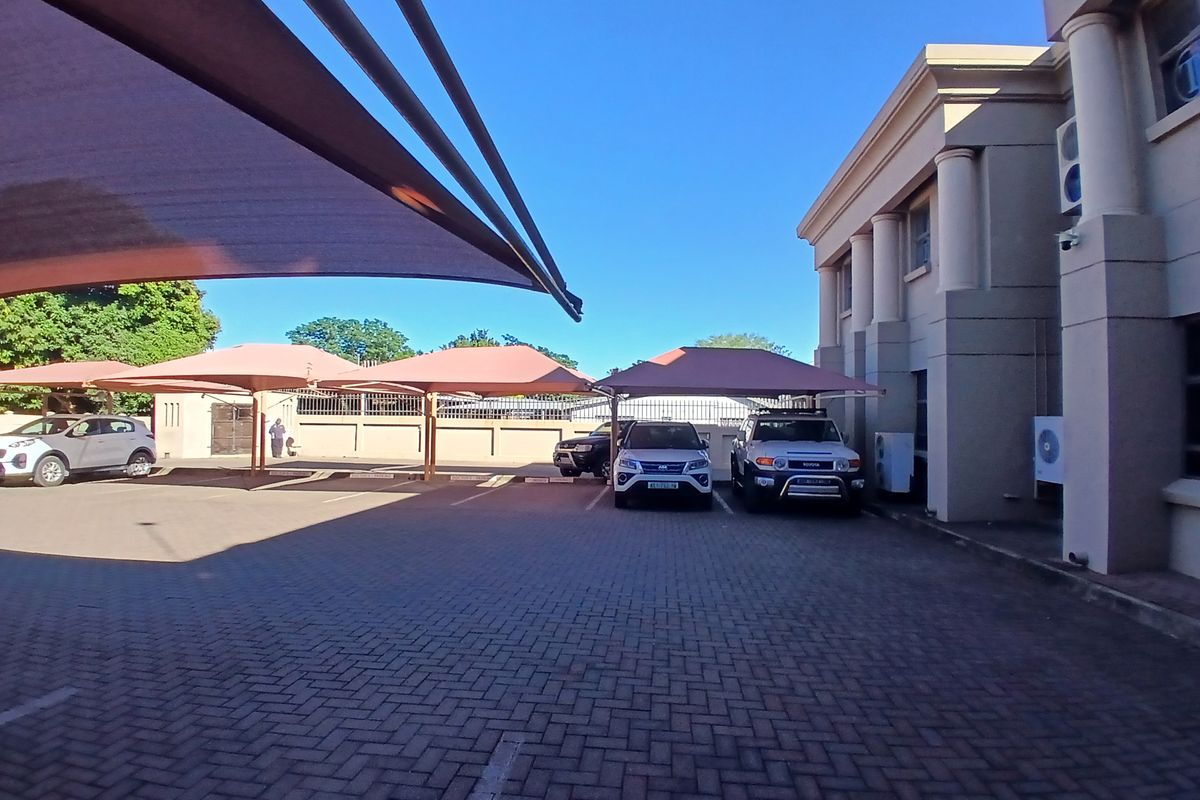 Exterior view of the office property featuring a paved parking area with shade cloth carports and architectural columns.