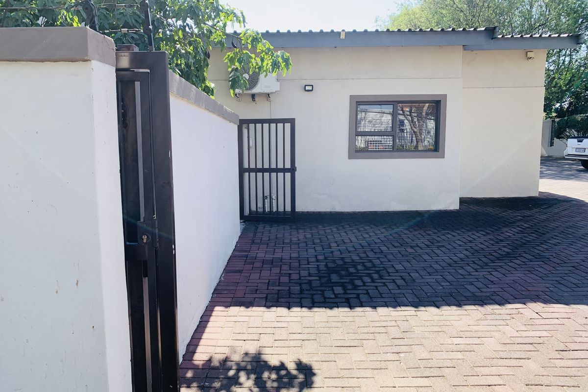 Rear exterior view featuring a paved driveway, security gate, boundary wall with electric fencing, and an external air conditioning unit.