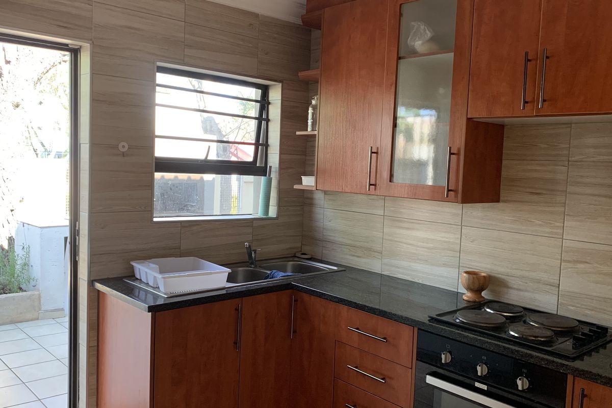 A functional kitchen featuring wood-finish cabinetry, granite countertops, a built-in oven and hob, and a tiled backsplash with direct access to an outdoor patio area.