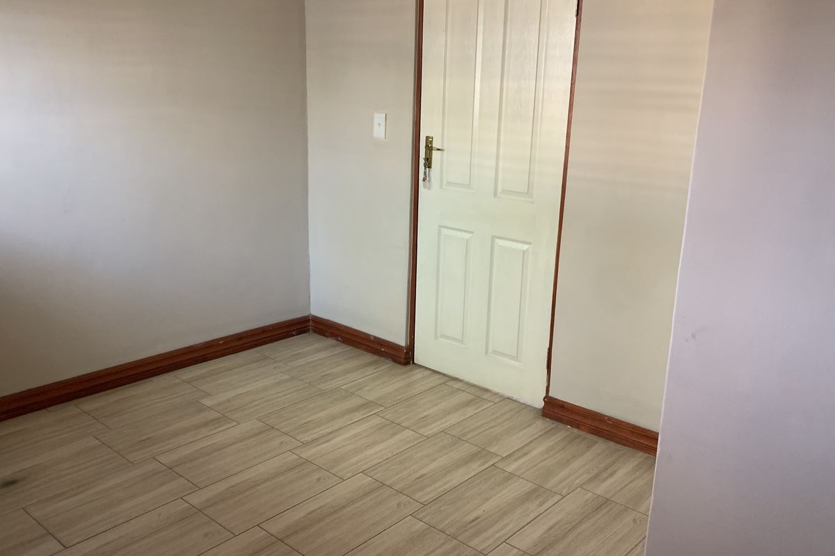 A clean, empty bedroom featuring neutral wall paint, wood-look tiled flooring, and a classic internal door.