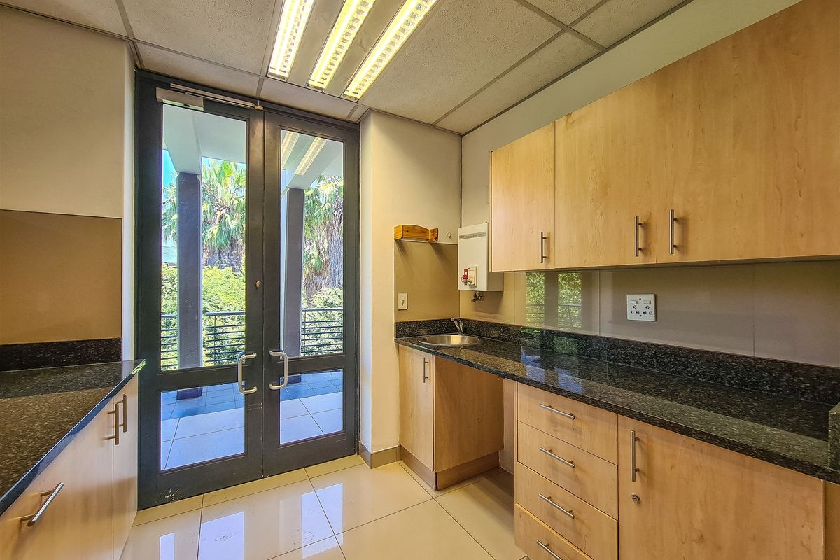 A clean, functional office kitchenette featuring granite countertops, light wood cabinetry, and direct access to an outdoor balcony area.