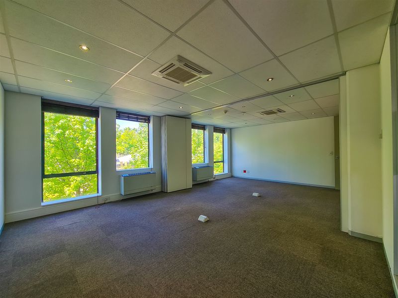 A spacious, empty office suite featuring a suspended ceiling, recessed lighting, integrated air conditioning, and large windows providing ample natural light.