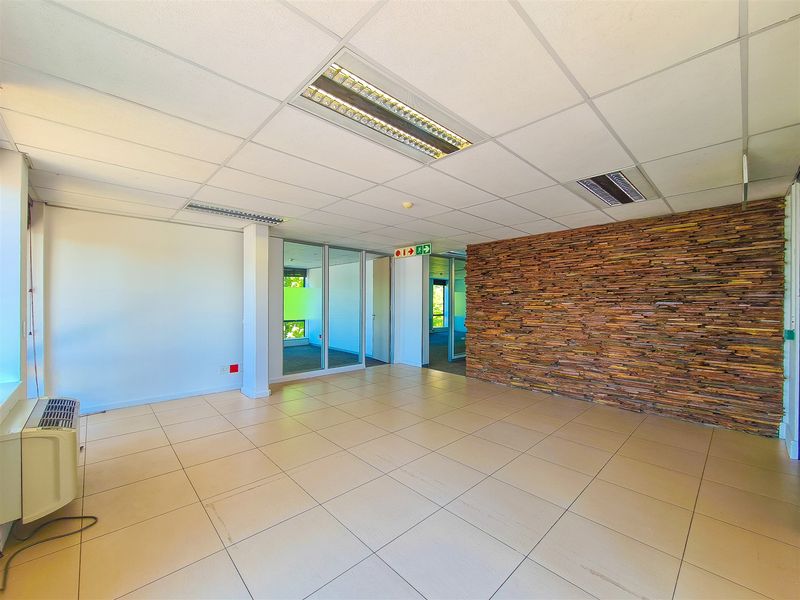 Spacious open-plan office area featuring a decorative stone feature wall, ceramic tile flooring, suspended ceilings, and glass partitions for a modern professional workspace.