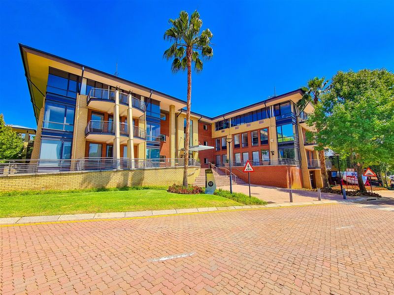 A modern multi-story office building featuring a brick and glass facade, private balconies, and a well-maintained landscaped entrance area.