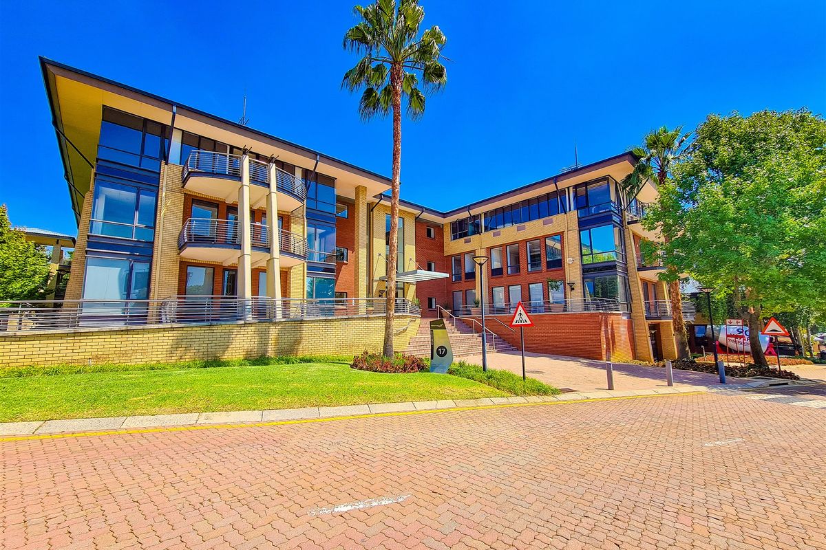 A modern multi-story office building featuring a brick and glass facade, private balconies, and a well-maintained landscaped entrance area.