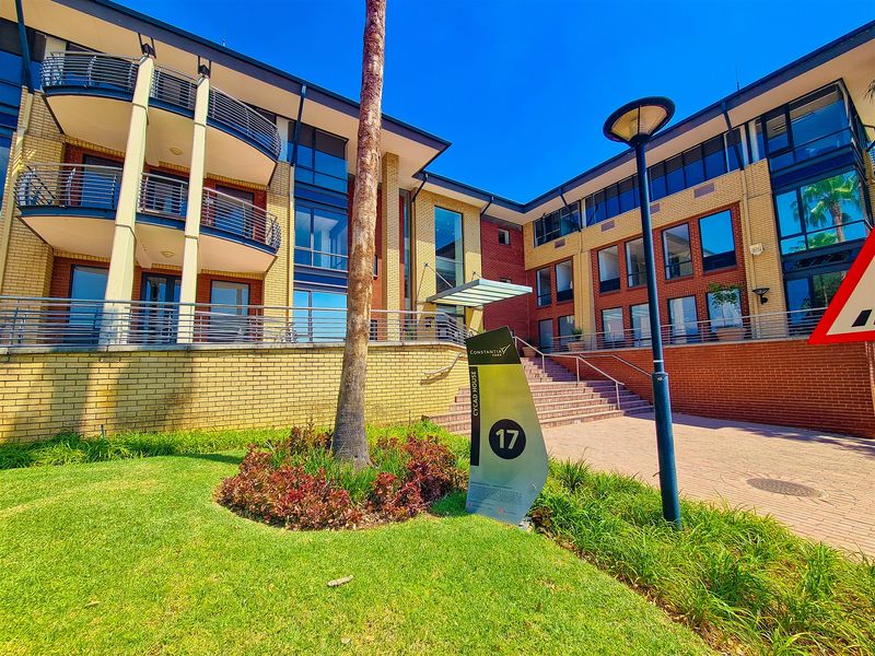 Front exterior view of a modern office building featuring brick facade, balconies with metal railings, and well-maintained landscaped grounds.