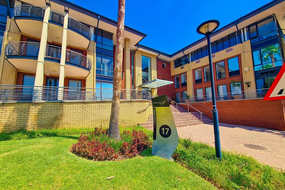 Front exterior view of a modern office building featuring brick facade, balconies with metal railings, and well-maintained landscaped grounds.