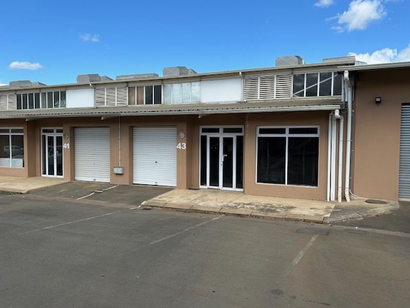 Front elevation of a commercial unit featuring roller shutter doors, glass entrance doors, and dedicated asphalt parking space.