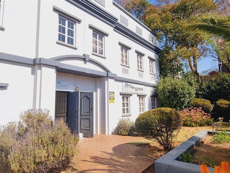 Front exterior view of a multi-story office building featuring a paved entrance, security gate, and well-maintained landscaped garden area.
