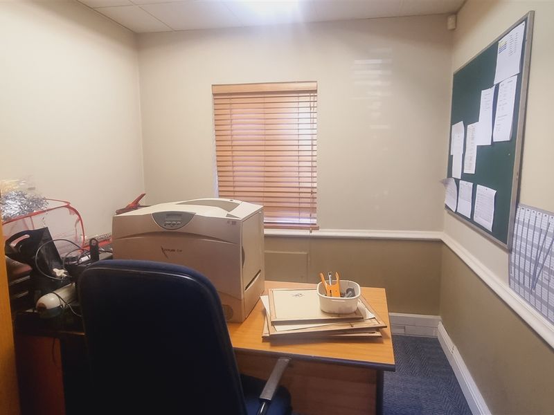 A functional office space featuring carpeted flooring, a suspended ceiling, and wooden window blinds, providing a practical environment for professional work.
