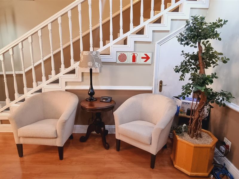 An office entrance area featuring a classic staircase with a white balustrade, laminate flooring, and a convenient under-stair storage cupboard.