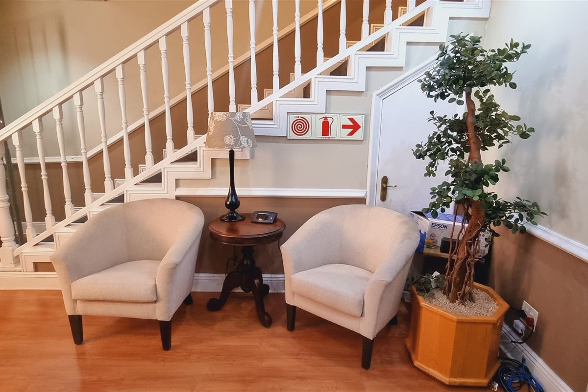 An office entrance area featuring a classic staircase with a white balustrade, laminate flooring, and a convenient under-stair storage cupboard.