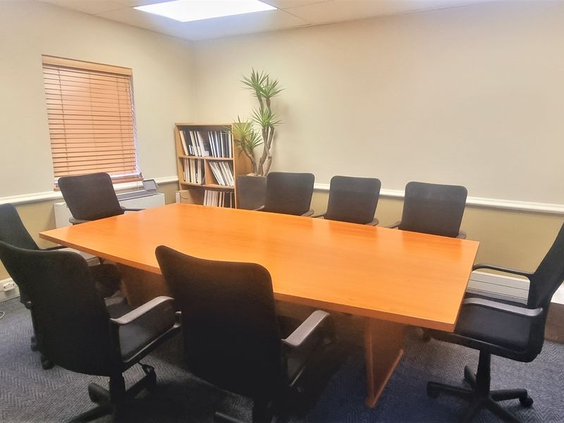 A functional office meeting room featuring carpeted flooring, chair rail molding, and recessed ceiling lighting, suitable for professional use.