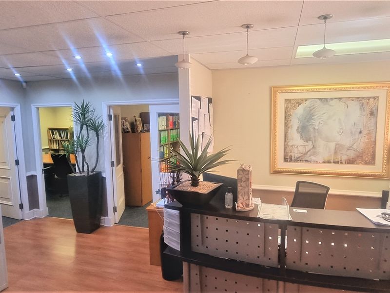 A functional office reception area featuring a built-in desk, suspended ceiling with recessed lighting, and laminate flooring, providing a professional entry space.
