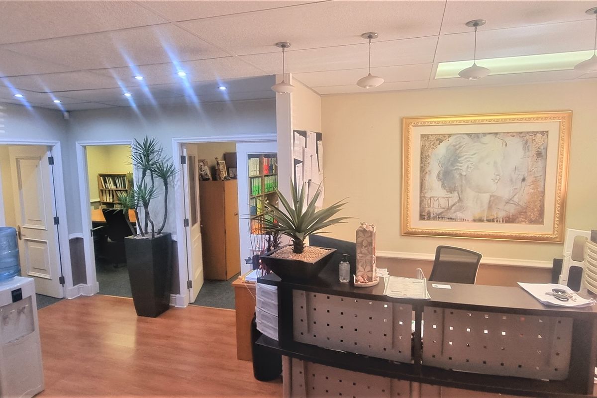 A functional office reception area featuring a built-in desk, suspended ceiling with recessed lighting, and laminate flooring, providing a professional entry space.