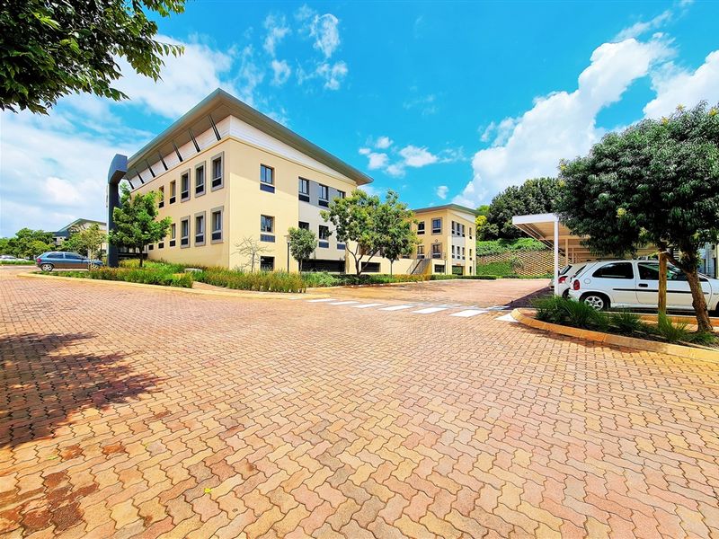 A well-maintained multi-story office building featuring a paved driveway, covered parking bays, and established landscaping in a professional business park setting.